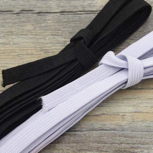 May include: Two spools of elastic, one black and one white. The elastic is folded and stacked on a wooden surface.