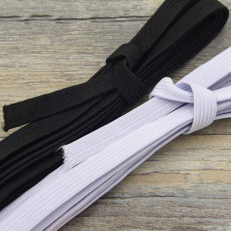 May include: Two spools of elastic, one black and one white. The elastic is folded and stacked on a wooden surface.