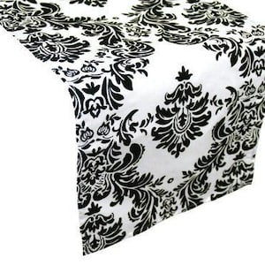 May include: Black and white damask table runner with a floral pattern. The runner is made of a soft, smooth fabric and is perfect for adding a touch of elegance to any table setting.