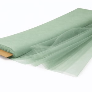 May include: A roll of sage green tulle fabric, partially unrolled, resting on a brown cardboard core. The sheer material is displayed against a white background, showcasing its delicate texture and color. Ideal for crafting and decorative projects.