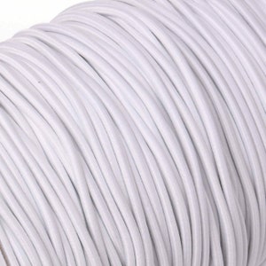 May include: A tightly wound spool of white elastic cord. The cord is made of a flexible, stretchy material and is tightly coiled, creating a dense, textured surface. The color is a bright, clean white, suitable for various crafting and sewing projects.