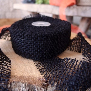 May include: A roll of black burlap ribbon with frayed edges. The ribbon is rolled up and tied with a white plastic spool.