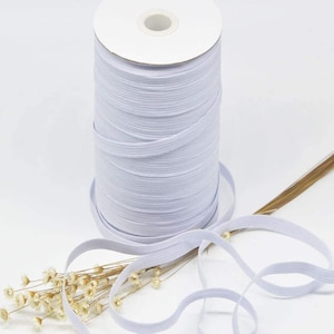 May include: A spool of white elastic cord, wound around a cardboard tube. The elastic cord is lying on a table with a sprig of dried flowers.
