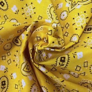 May include: A bright yellow fabric featuring a repeating bandana print in black and white. The pattern consists of intricate paisley shapes, small floral motifs, and geometric diamond outlines distributed evenly across the vibrant yellow surface.