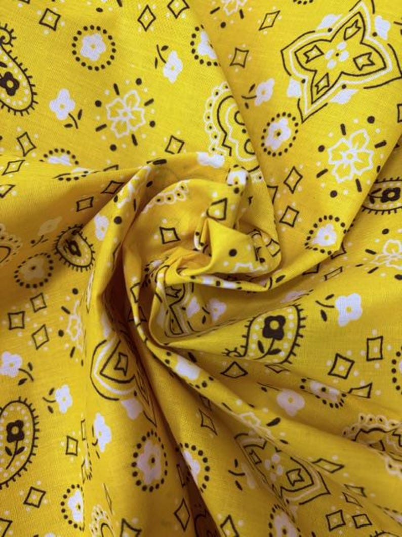 May include: A bright yellow fabric featuring a repeating bandana print in black and white. The pattern consists of intricate paisley shapes, small floral motifs, and geometric diamond outlines distributed evenly across the vibrant yellow surface.