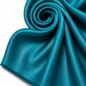 May include: A teal satin fabric scarf featuring a smooth, lustrous finish and a tightly coiled spiral design at the top. The edges of the fabric are finished with a straight stitched hem and a short, delicate fringe along the bottom border.
