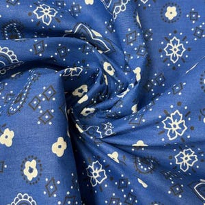 May include: A blue fabric featuring a repeating white and black bandana print. The pattern consists of intricate paisley shapes, small four-petaled flowers, and diamond outlines arranged in a classic symmetrical layout across the textile surface.