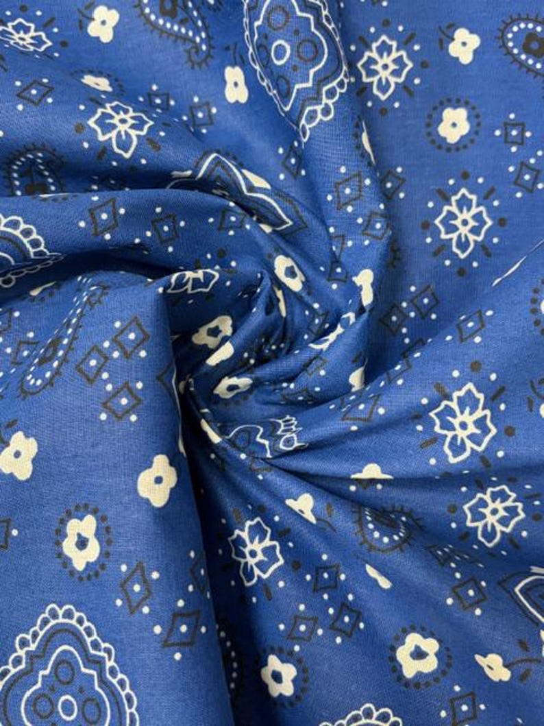 May include: A blue fabric featuring a repeating white and black bandana print. The pattern consists of intricate paisley shapes, small four-petaled flowers, and diamond outlines arranged in a classic symmetrical layout across the textile surface.