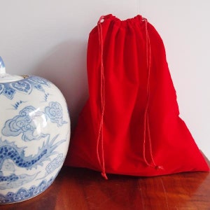 May include: A red velvet drawstring bag with a white background. The bag is empty and has a drawstring closure.