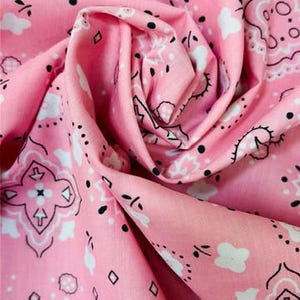 May include: A light pink fabric featuring a repeating bandana pattern in white and black. The design includes intricate floral motifs, small diamond shapes, and paisley elements printed across the surface of the soft, folded textile material.