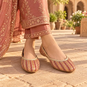 May include: A pair of flat shoes featuring a multi-colored striped pattern with intricate embroidery and gold-toned trim. The shoes are worn with matching dusty rose trousers that have detailed gold floral embroidery along the hem and cuffs.