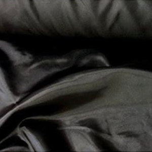 May include: Black satin fabric with a smooth, silky texture. The fabric is folded and draped, showing its luxurious sheen.