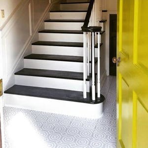 May include: A white and black staircase with a white railing and a yellow door. The floor is tiled with a geometric pattern in gray and white.