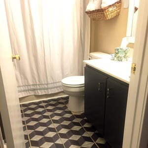 Puede incluir: Un ba&ntilde;o con una cortina de ducha blanca, un inodoro blanco, un armario azul oscuro con una encimera blanca y un suelo de baldosas geom&eacute;tricas en blanco y negro.