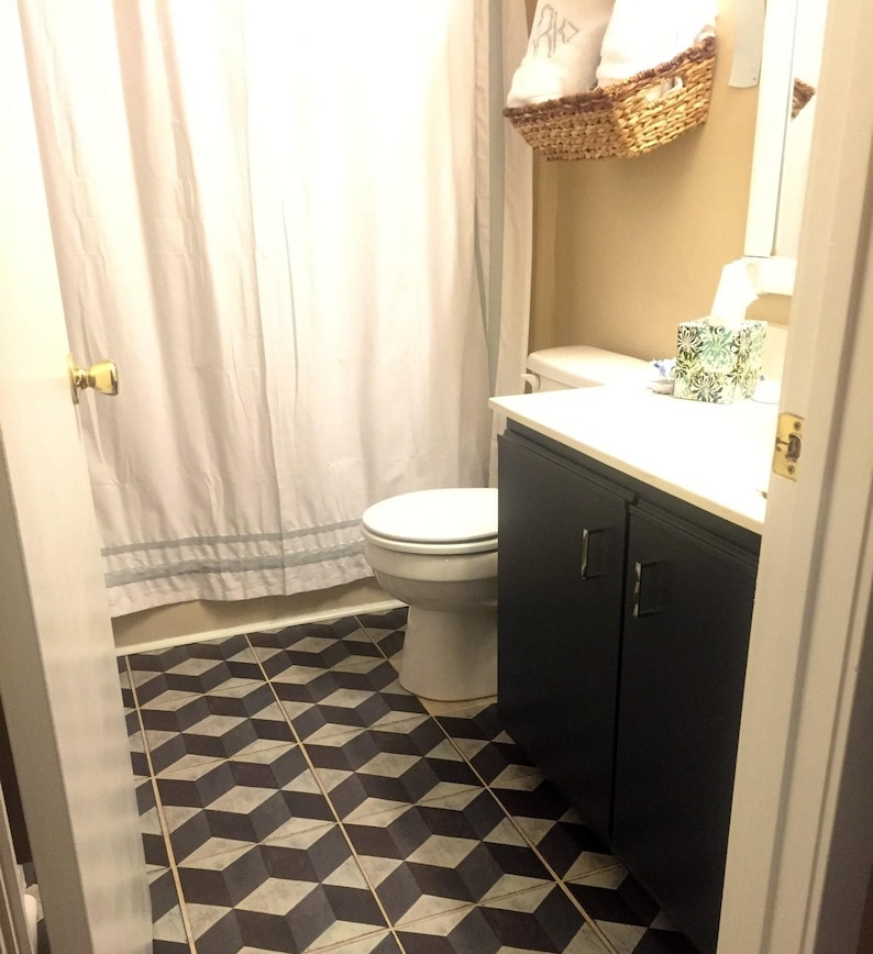 Puede incluir: Un ba&ntilde;o con una cortina de ducha blanca, un inodoro blanco, un armario azul oscuro con una encimera blanca y un suelo de baldosas geom&eacute;tricas en blanco y negro.
