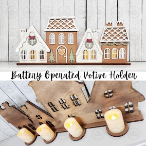 May include: A battery-operated votive holder shaped like a village of gingerbread houses. The houses are made of wood and painted in white, brown, and green. The text "Battery Operated Votive Holder" is displayed below the houses.