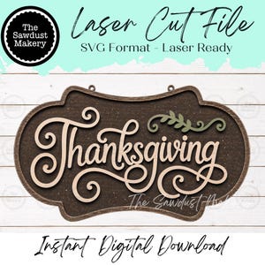 May include: A laser cut file design featuring a dark brown oval sign with the word Thanksgiving in light beige script lettering. A small green leafy branch accent sits above the text. The file includes SVG format and is laser ready.