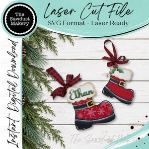 May include: Two Christmas boot ornaments featuring red and black patterns, white faux fur trim, and gold buckles. One boot displays the name Ethan in green script. Both ornaments are topped with red and black buffalo plaid fabric bows.