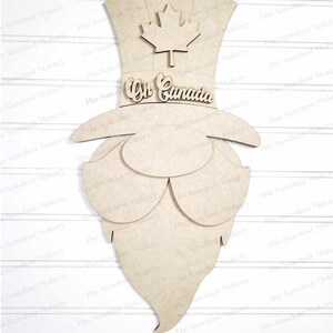 May include: A wooden cutout of a Canadian gnome wearing a top hat with a maple leaf on top. The hat has the words "Oh Canada" written on it. The gnome has a long beard.