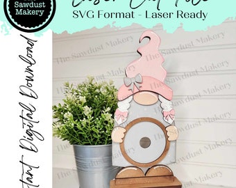 May include: A laser cut file for a gnome with a pink hat, grey body, and a round wooden base. The file is in SVG format and is ready to be used with a laser cutter. The text "The Sawdust Makery" is visible in the image.