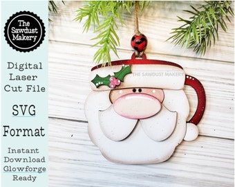 May include: A wooden Santa Claus mug ornament with a red hat, white beard, and black eyes. The ornament is decorated with holly and a red and black checked bow. The text "THE SAWDUST MAKERY" is printed on the mug.