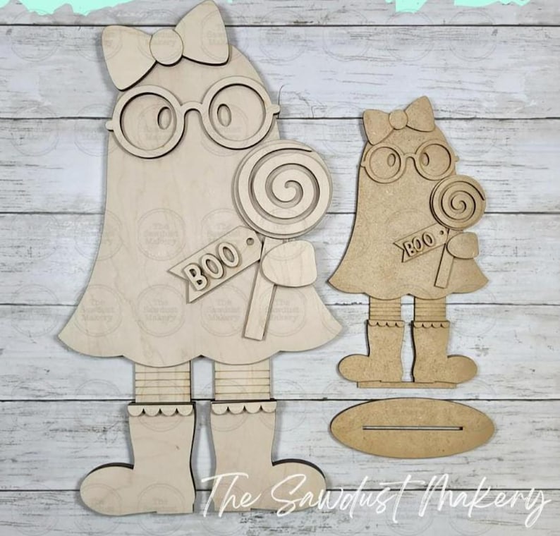 May include: Two unfinished light-colored wood ghost cutouts. Each ghost features a bow, round glasses, a lollipop, and a tag with the word BOO. The larger ghost has legs and boots, while the smaller ghost includes a separate oval wooden base.