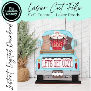 May include: A blue truck with a white bed and a red "COCOA" mug filled with marshmallows. The truck has a sign that says "LET'S GET COZY" and is on a wooden stand.