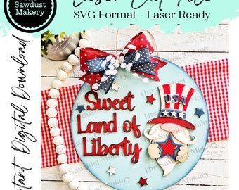 May include: A blue and white wooden sign with the text "Sweet Land of Liberty" and a red, white, and blue Uncle Sam gnome with a star on his hat. The sign is decorated with a red, white, and blue bow and stars.