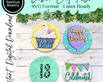 May include: Four round wooden signs with a birthday theme. The signs feature a cupcake with the text "Make a Wish", a purple balloon with the text "Happy Birthday", a teal sign with the number "13" and the text "Happy Birthday", and a white sign with the text "Celebrated" and colourful flags.