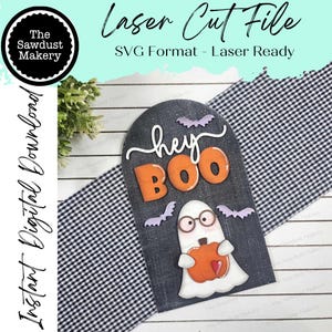 May include: A black and white laser cut file for a Halloween sign with the text "hey BOO" and a ghost holding a pumpkin. The ghost has a heart on its chest and is wearing glasses.