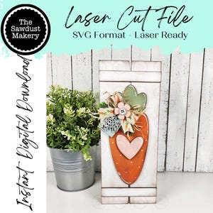 Può includere: Decorazione in legno a forma di carota con un ritaglio a forma di cuore e accenti floreali. La carota è arancione con puntini bianchi e lo sfondo è un design a doghe di legno bianco. Il testo sull'immagine recita "Laser Cut File" e "Instant Digital Download."