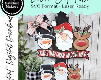 May include: A laser cut file featuring Christmas-themed decorations. The design includes a snowman, Santa Claus, and a reindeer, with the text "CHRISTMAS CHEER WELCOME HERE" on a banner. The file is labeled "SVG Format - Laser Ready."
