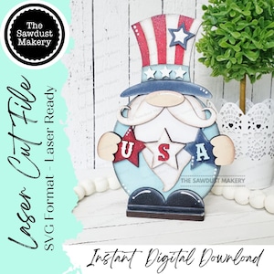 May include: A wooden gnome wearing a red, white, and blue hat with stars and holding a sign that says "USA". The gnome is holding two stars in its hands. The gnome is a laser cut file.