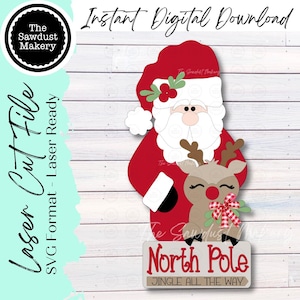 May include: A digital laser cut file featuring a red and white Santa Claus holding a tan reindeer with a red nose and a red and white checkered bow. Below them is a sign with the text North Pole and Jingle All The Way. The design includes holly accents.