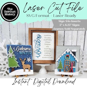 May include: A display of laser-cut winter-themed signs. One sign reads "Welcome Winter" with a deer and tree. Another features the word "Winter" and a list of winter words. The third sign is a blue house with a wreath and skis. The text "Laser Cut File" is also visible.