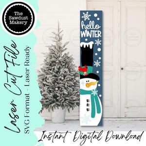 May include: A vertical wooden sign featuring a snowman design with the text "hello WINTER". The snowman has a black top hat, a teal scarf, and a carrot nose. The sign is decorated with snowflakes and a red cardinal. A small Christmas tree is to the left.