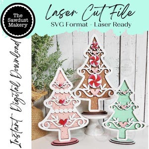 Könnte beinhalten: Drei lasergeschnittene Weihnachtsbaumdekorationen aus Holz in Rosa, Braun und Grün. Jeder Baum hat einen dekorativen weißen Rand, Herzakzente und einen Sockel. Das Bild enthält den Text "Laser Cut File" und "Instant Digital Download."