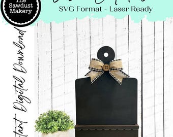 May include: A black laser-cut file design with a decorative bow and button. The design includes a small shelf and a circular handle. The text reads "Laser Cut File" and "SVG Format - Laser Ready". The Sawdust Makery logo is also visible.