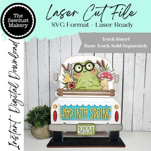 Può includere: Un inserto per camion in legno tagliato al laser con una rana con gli occhiali, funghi e giunchi. Il camion è bianco con dettagli rossi e il testo "Hop Into Spring" e "Ribbit". Il logo Sawdust Makery è in alto a sinistra.