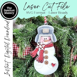 May include: A wooden snowman ornament with a red scarf, snowflake, and buttons. The snowman wears a gray hat with "BRRR" on it. The ornament is hanging in front of a Christmas tree. Text on the image says "Laser Cut File" and "Instant Digital Download."