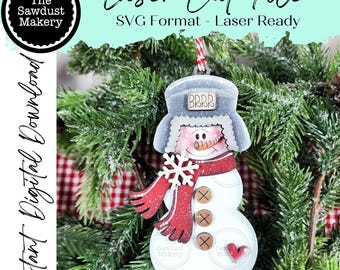 May include: A wooden snowman ornament with a red scarf, snowflake, and buttons. The snowman wears a gray hat with "BRRR" on it. The ornament is hanging in front of a Christmas tree. Text on the image says "Laser Cut File" and "Instant Digital Download."