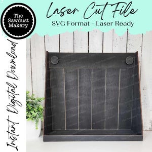 May include: A black wooden shelf with a slanted front and a back panel with vertical grooves. The shelf has two round metal accents on the top edge. The shelf is sitting on a white wooden surface. "Laser Cut File" and "SVG Format - Laser Ready" are written in white text on a light blue background.