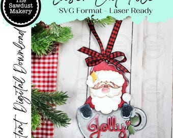 May include: A festive laser-cut Christmas decoration depicting Santa Claus in a mug, with the word "Jolly" in red script. It includes a red and black checked ribbon. The text "Laser Cut File" and "Instant Digital Download" are also visible.
