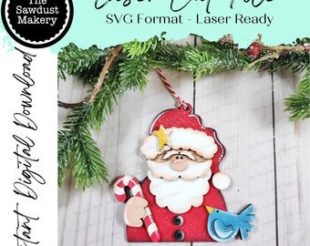 May include: A laser-cut wooden Christmas ornament shaped like Santa Claus, with a red glittery hat and coat. The ornament features a candy cane, a blue bird, and a star. The image includes the text "Laser Cut File" and "Instant Digital Download."