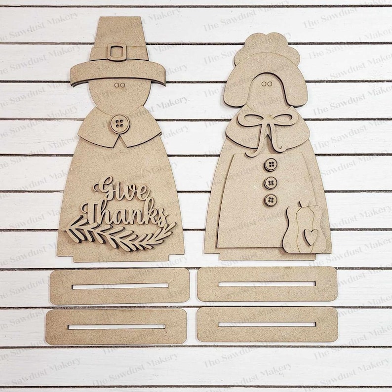 May include: A wooden craft kit featuring a pilgrim couple with the words "Give Thanks" on the man's outfit. The kit includes four separate pieces for the couple's bodies and a base.