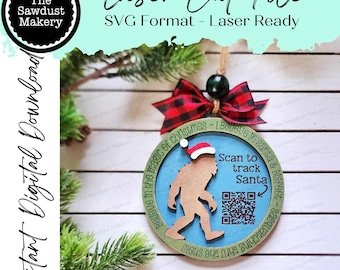 May include: A laser-cut Christmas ornament featuring a Bigfoot design wearing a Santa hat. The ornament has a blue center with the text "Scan to track Santa" and a QR code. It is decorated with a red and black plaid bow and the text "Believe in the magic of Christmas".