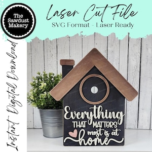 May include: A laser cut file for a wooden home sign with the text "Everything that matters most is at home". The sign is black with a brown roof and a heart in the center of the text.