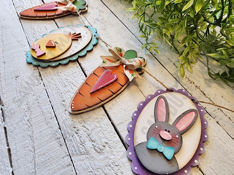 May include: A wooden Easter garland with a chick, carrots, and a bunny. The garland is painted in bright colors and has a scalloped edge.