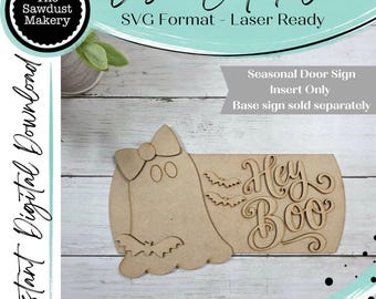 May include: A laser-cut wooden sign insert featuring a ghost shape with a bow on its head, two small bats, and the text "Hey Boo" in a cursive font. The piece is designed for a seasonal door sign and is presented as a digital SVG file.
