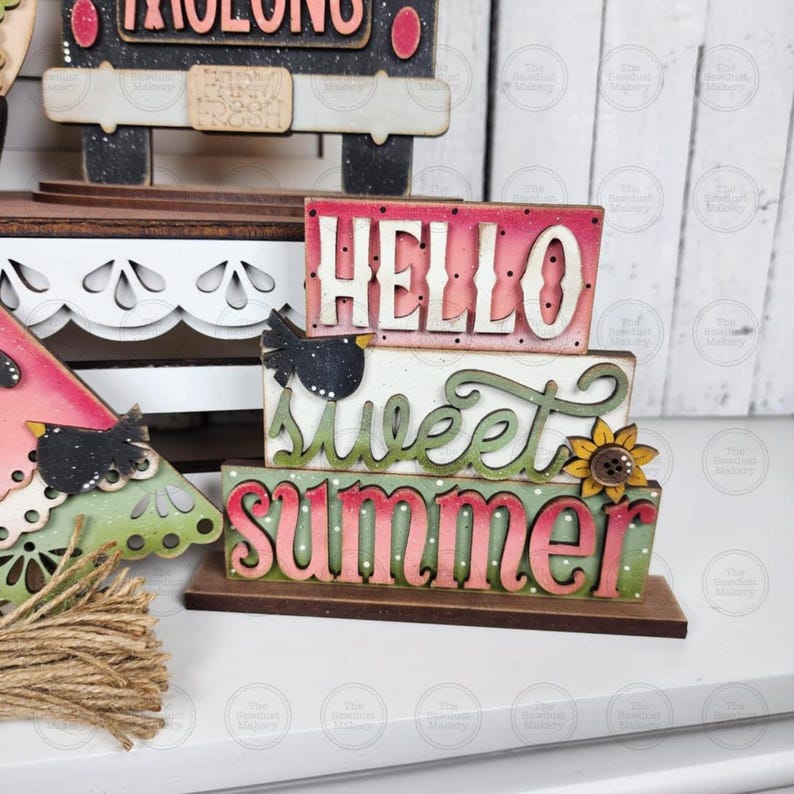 May include: A wooden summer-themed decoration with the words "Hello Sweet Summer" in layered, colorful lettering. The design includes a small bird and a sunflower accent, with a watermelon slice nearby. The base is brown.